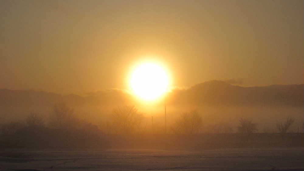 早春を思わせるような神々しい朝日を見ることができました 午前6時45分東の空から太陽が昇り始めました 気温も低く霧が立ち込めていて遠くの山並みがうっすらと見え道路の桜並木もかすかに見える幻想的な朝の風景となりました まだ雪が解けない田んぼもオレンジ色に染まっています カメラではその美しさをとらえきれませんが春を感じてほしい