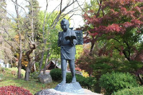 今朝はあいにくの雨　昨日烏帽子山八幡宮参集殿前の庭で二宮金次郎像を撮りました　かつてどの校庭にもありましたが今は見ることできない像の一つです　像の後ろにかつて源泉の小高い山にあった六角堂も見えます　もう少しで鮮やかなイチョウの木も見ることができる場所です